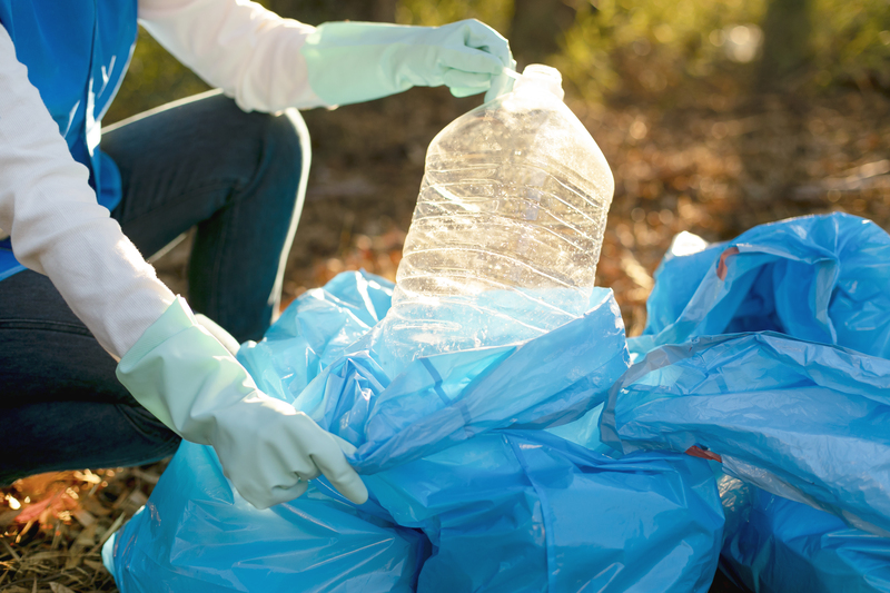 Pessoa reciclando uma garrafa de plástico, colocando em um saco de lixo.